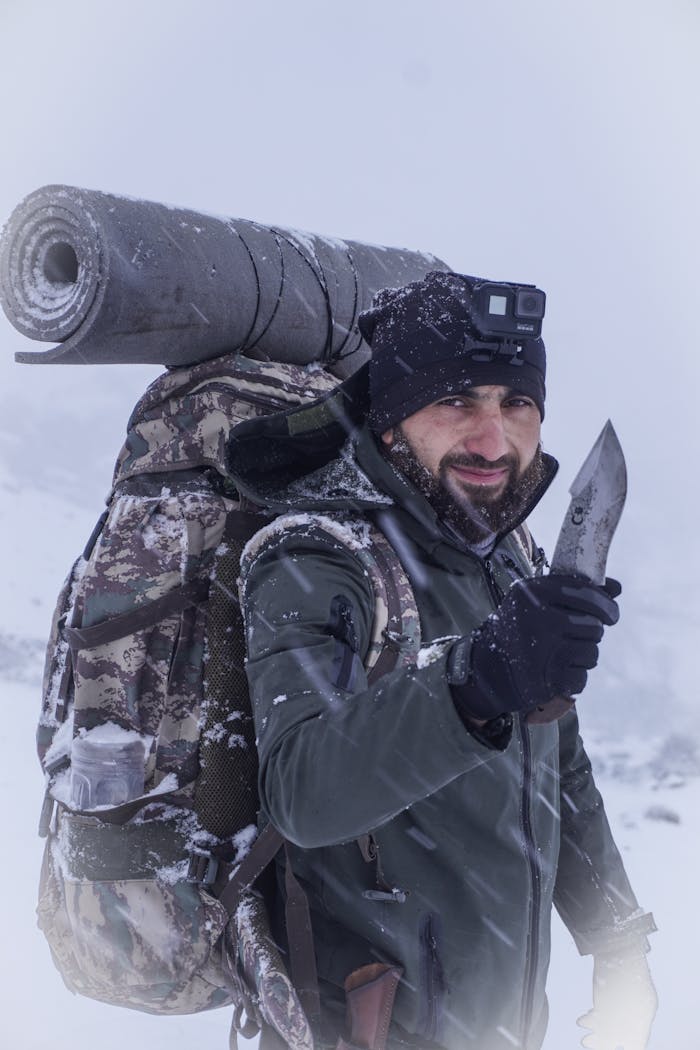 Man with backpack and knife in snowy wilderness, ready for adventure.